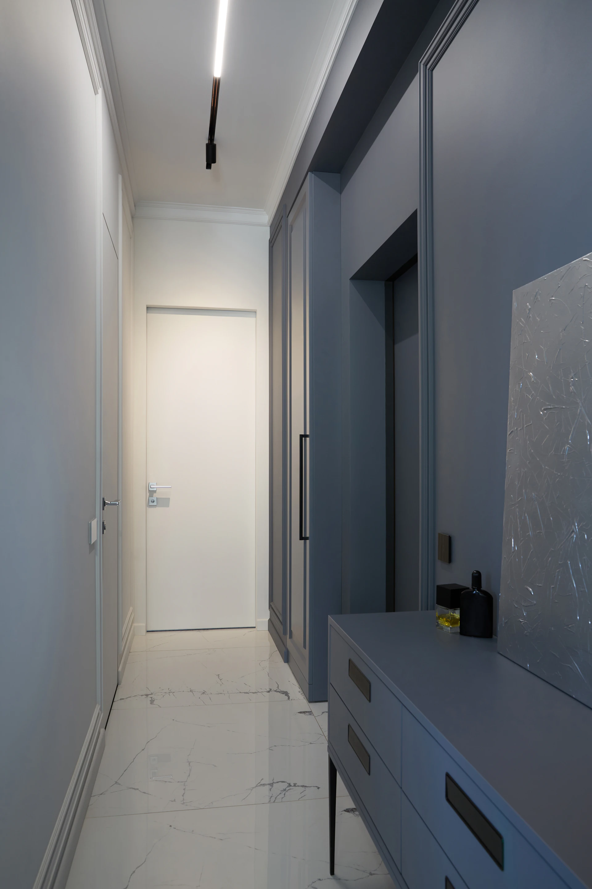 Narrow entrance hallway of a penthouse with marble flooring, grey-blue built-in cabinetry and a single strip of ceiling light