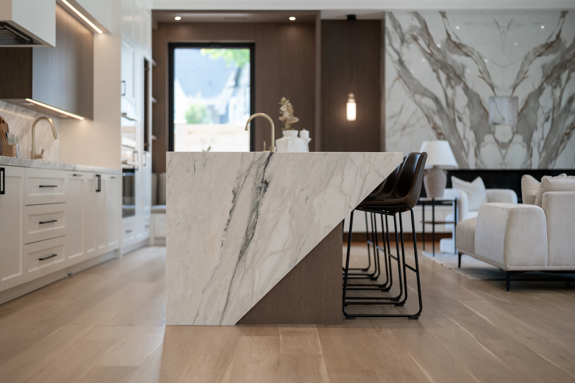 Open kitchen with a Calacatta marble island, walnut cabinetry and brass fixtures opening onto the living area